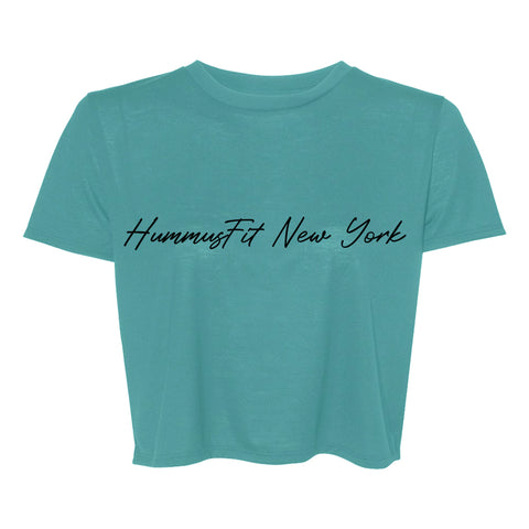 The Turquoise Hummus Fit Script Crop Tee features four-way stretch fabric and HummusFit New York in black cursive across the chest.