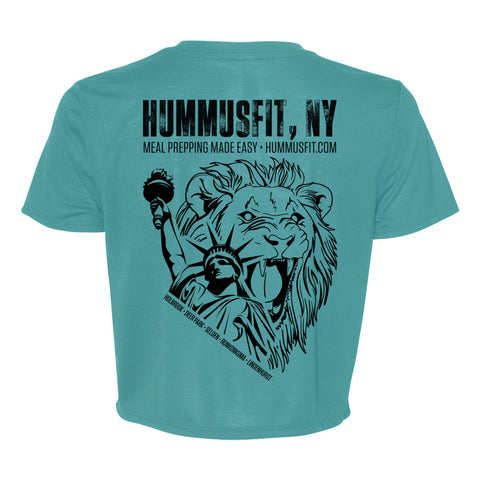 The Turquoise Hummus Fit Script Crop Tee features a Statue of Liberty and lion design with “HUMMUSFIT, NY” above and “Meal Prepping Made Easy · hummusfit.com” below, crafted from four-way stretch fabric.