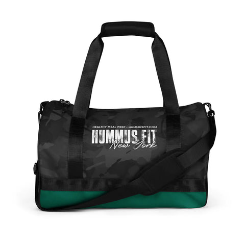 The Hummus Fit Cylinder Black Camo Gym Bag is water-resistant, with black handles, an adjustable shoulder strap, and HUMMUS FIT New York Healthy Meal Prep - HUMMUSFIT.COM printed in white on the front.