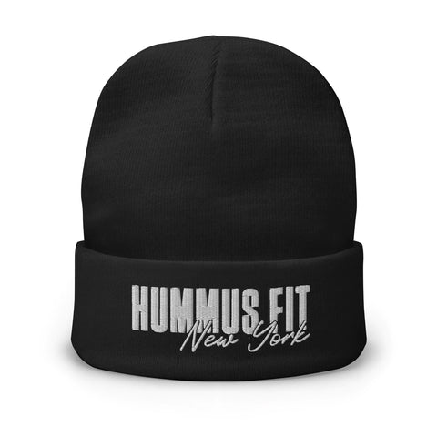 The Hummus Fit NY Embroidered Beanie is a black cotton blend hat with HUMMUS FIT in bold white letters and New York in cursive embroidered on the folded brim.