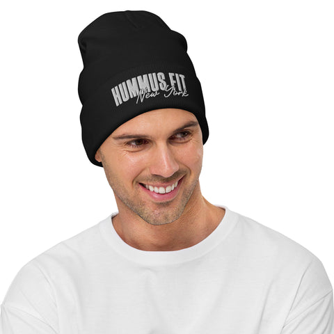 A smiling man wears the Hummus Fit NY Embroidered Beanie in black cotton blend with white stitching, paired with a plain white shirt.