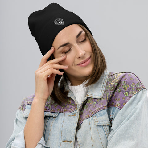A woman smiles softly with her eyes closed, gently touching her temple while wearing a Unisex Embroidered Beanie and a denim jacket with a purple and green patterned yoke against a plain gray background.