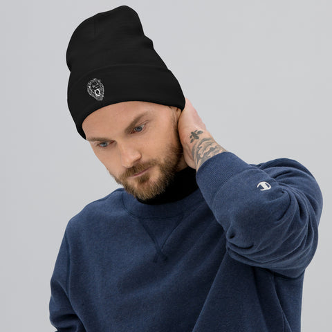A bearded man wearing the Unisex Embroidered Beanie featuring a lion emblem and a blue cotton blend sweatshirt touches his neck, gazing down thoughtfully against a light gray background.