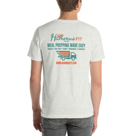 A man wears the Unisex Hummus Fit New York Ash T-Shirt, a comfy 100% cotton light gray tee with colorful graphics and text on the back promoting Hummus Fit meal prep, featuring a delivery truck and www.hummusfit.com.