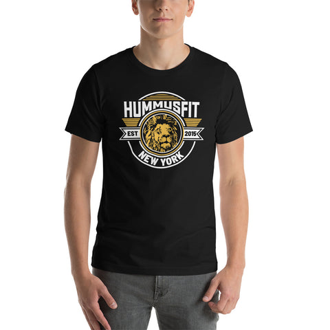 A person wearing the Unisex Gold Hummus Fit T-Shirt, a soft cotton black tee with a graphic lion’s head and “HummusFit Est 2015 New York!” in white and yellow, stands facing forward with hands relaxed by their sides.