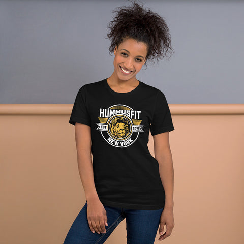 Smiling woman with curly hair wears a comfortable Unisex Gold Hummus Fit T-Shirt, standing in front of a simple, two-tone background.