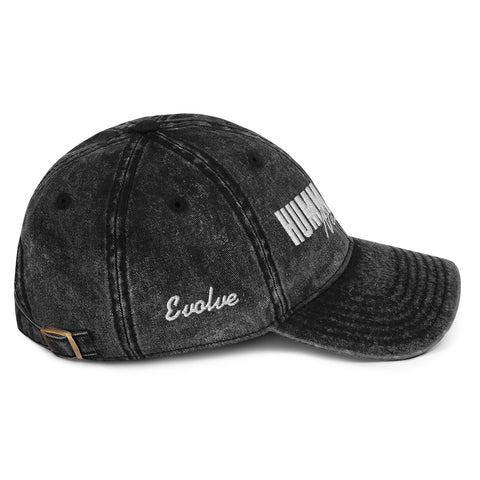 The Hummus Fit Vintage Cotton Twill Cap is a black dad hat with “Evolve” in white script on the side, bold white text on the front, a curved brim, and an adjustable strap. Made from cotton twill for comfort and style.