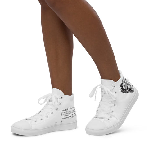 A person with medium brown skin wears Women’s high top canvas shoes, featuring black graphic designs and text details, standing against a plain white background.
