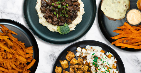 A black plate with mashed potatoes topped with beef stew, garnished with chopped green onions, and two pieces of broccoli on the sides.