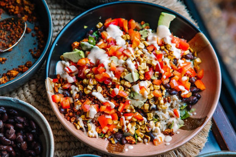 A black plate with white rice topped with ground meat, shredded cheddar cheese, jalapeño slices, and diced red onion, served with a small cup of creamy orange sauce on the side.