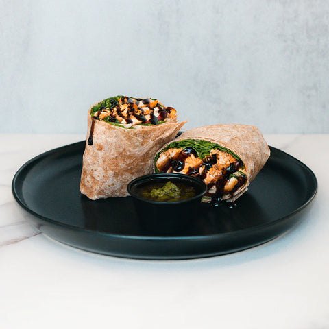 Two delicious chicken wraps drizzled with dark sauce, served on a black plate with a side of green sauce.