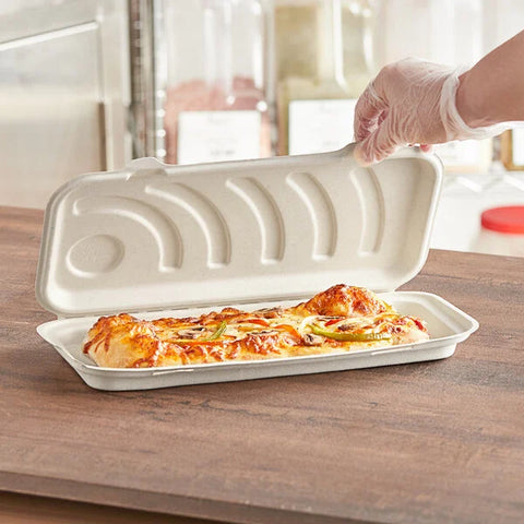 A hand in a glove opens a Flatbread Box from a 250 ct pack, revealing a cheesy baked sub sandwich topped with peppers and onions, sitting on a wooden counter.