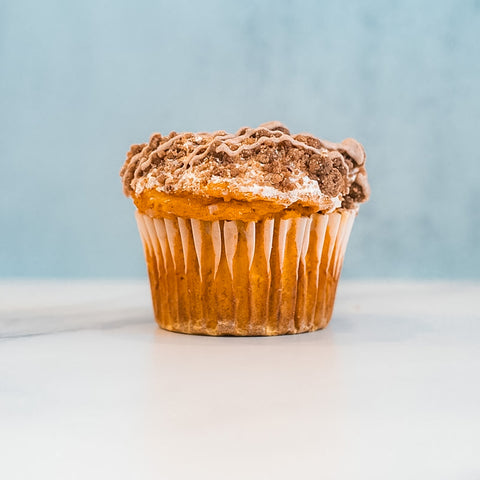 A Basic Baddie Buffin Muffin with chocolate frosting and sprinkles sits on a white surface against a light blue background, making for a delicious, high-protein snack.