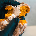 Wearing black gloves, someone pulls apart a crumbly, orange-yellow Basic Baddie Buffin Muffin—a pumpkin spice protein treat dusted with powdered sugar and packed with irresistible flavor for a satisfying, high-protein snack.