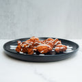 A black plate with pieces of fried chicken, drizzled with white sauce, placed on a white marble surface with a light gray background.