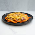 The FitWendy Double Stack Bowl features baked sweet-potato fries topped with ground beef, chopped bacon, cheddar cheese, and yellow sauce—served on a black plate for a high-protein meal against a light gray background.