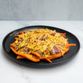 The FitWendy Double Stack Bowl features baked sweet-potato fries with ground beef, shredded cheddar, bacon strips, and yellow sauce for a high-protein meal, served on a black plate over white marble with a gray background.