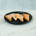 Four quesadilla wedges with visible filling are arranged in a row on a round black plate, set on a white marble surface with a light gray background—perfect for meal prep or as part of your HFit Signature Fold.