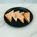 Four triangular quesadilla slices with visible cheese and vegetables inside are neatly arranged on a round black plate set on a white marble surface, creating a dish that’s perfect for meal prep with HFit Signature Fold or as part of your Signature Chicken Fold.