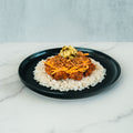A black plate with white rice topped with BBQ Meltdown, shredded cheddar cheese, and chopped pickles is set on a white marble surface against a light background—a delicious option for healthy meal prep or anyone seeking a high-protein meal prep idea.