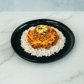 A black plate holds the BBQ Meltdown—a high-protein meal of white rice topped with BBQ chicken, shredded carrots, chopped pickles, and crispy fried onions—creating a colorful dish set on a marble surface.