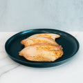 Three cooked, seasoned Baked Herbed Tilapia 1lb Competition Approved fillets are presented on a dark blue plate atop white marble—ideal for meal prep or supporting your weight loss journey.
