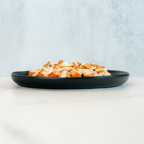 A black plate featuring a serving of diced, grilled chicken breast—ideal for meal prep or as the protein in a Brookfield Chicken Bowl—rests on a light-colored marble surface against a softly blurred background.