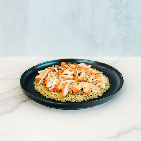 A black plate features a serving of rice topped with sliced Brookfield Chicken Bowl grilled chicken breast, sautéed onions, and crispy fried onions, all set on a marble surface with a light gray background—ideal for quick and convenient meal prep.