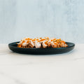 Try this rewritten sentence incorporating the product name: Fit-Fil-A features sliced grilled chicken breast topped with shredded cheese and herbs, served alongside baked waffle fries on a black plate set on a white marble surface against a light blue background—an inviting and healthy dinner option.