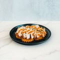 A Fit-Fil-A waffle, topped with sliced smoked chicken breast, shredded cheese, fresh herbs, and a drizzle of sauce, is served on a black plate over white marble—perfect for a healthy dinner.