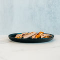 A black plate holds several Strongsville Chicken Ranch Fold quesadillas filled with melted cheese and slices of HALAL Turkey bacon, set on a white marble surface against a light blue background—perfect for anyone seeking a delicious, high protein meal.