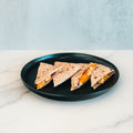 Three triangular slices of the Strongsville Chicken Ranch Fold, filled with melted cheese, halal turkey bacon, and other savory ingredients, are arranged on a round black plate set on a white marble surface with a light gray background.