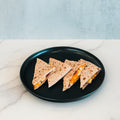 Four triangular slices of the Strongsville Chicken Ranch Fold, filled with melted cheese and savory halal turkey bacon, are served on a black plate atop a marble countertop with a light gray background—a delicious high-protein meal perfect for any time of day.