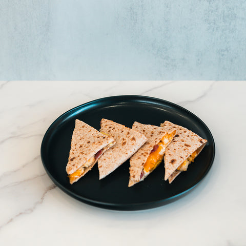 Four triangular slices of the Strongsville Chicken Ranch Fold, filled with melted cheese and savory halal turkey bacon, are served on a black plate atop a marble countertop with a light gray background—a delicious high-protein meal perfect for any time of day.