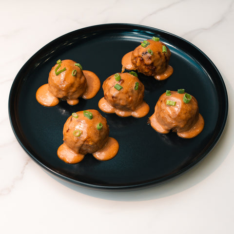 Keto BBQ Chicken Meatballs—juicy, high-protein meatballs in a tangy BBQ sauce—are served on a black plate, making them the perfect low-carb keto meal for anyone seeking delicious flavor and nutrition.