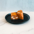 The Spicy Buffalo Wrap, sliced in half to reveal its flavorful filling, rests on a black plate placed on white marble with a light gray background—making it an ideal choice for healthy wraps or meal prep.