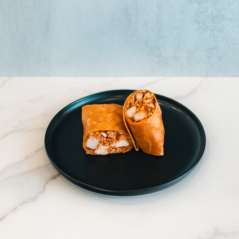 A black plate holds the Spicy Buffalo Wrap, sliced in half to showcase its seasoned chicken filling. Ideal for meal prep, the wrap is presented on a white marble surface with a light gray background.