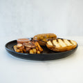 The Stacked and Jacked features a grilled hamburger bun, high-protein grass-fed beef cheeseburger patty, thick Idaho fries, and a dipping sauce, all served on a black plate atop a white surface.