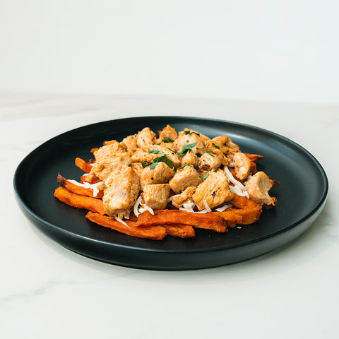 Lemon Pepper Chicken With Sweet Fries served on a black plate—cubed lemon pepper chicken over sweet potato fries, garnished with fresh herbs for a delicious, high-protein meal.
