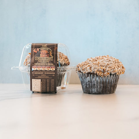 A Buffin Muffin - German Chocolate Cake with coconut topping sits next to a clear plastic pack containing another, both set against a light blue background—an indulgent treat that feels fitness-friendly.