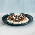 An Olympian Chicken Gyro Bowl featuring a black plate with rice, sliced meat, black olives, and crumbled white cheese, served with a side of white sauce.