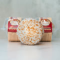 A VIP Buffin Muffin - Cookie Butter Tres Leches with white icing and orange sprinkles sits in front of a clear package of more muffins. A softly blurred background highlights the treat’s subtle cookie butter flavor.