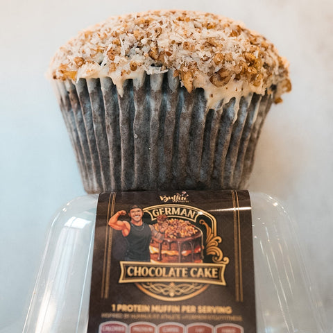 The Buffin Muffin - German Chocolate Cake is a large, fitness-inspired muffin with a crumbly coconut and nut topping in a clear container, featuring a muscular cartoon chef on the label.