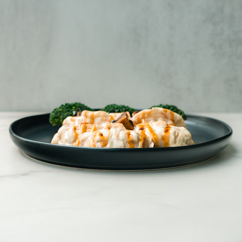 Savor Chicken Mushroom Pot Stickers with rich teriyaki flavor, served on a black plate with sauce and broccoli, set against a plain gray background.