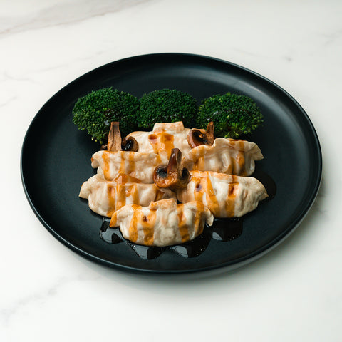 Chicken Mushroom Pot Stickers: Six savory dumplings with teriyaki sauce, mushrooms, and three broccoli florets served on a black plate atop white marble.