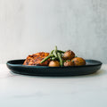 Baked Herb Chicken and Potatoes—roasted potatoes, green beans, and seasoned chicken breast on a black plate atop white marble—offers a high-protein meal prep option, perfect for healthy eating against a light gray background.