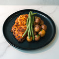 Baked Herb Chicken and Potatoes—a high-protein meal prep with roasted baby potatoes and green beans, served on a black plate atop white marble.