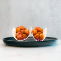 Two small tacos filled with honey garlic crispy chicken and purple cabbage are arranged upright on a dark plate against a light background, offering a flavorful twist perfect for high-protein meal prep enthusiasts.