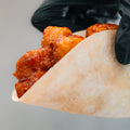 A gloved hand holds a soft tortilla filled with golden, saucy, crispy fried chicken pieces, capturing the irresistible appeal of a Honey Garlic Crispy Chicken Taco against a plain background.