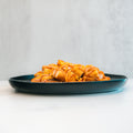 A dark plate holds a serving of "Closed on Sunday" Crispy Chicken Bowl with golden, crispy pieces drizzled in syrup—an inviting, macro-friendly lunch—set on a white surface against a light gray background.